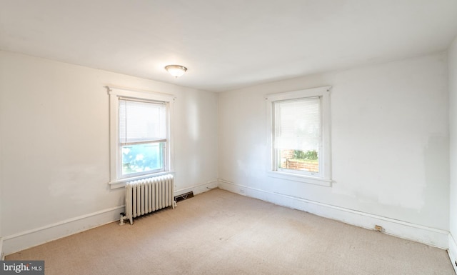 spare room featuring light carpet, radiator heating unit, and a wealth of natural light