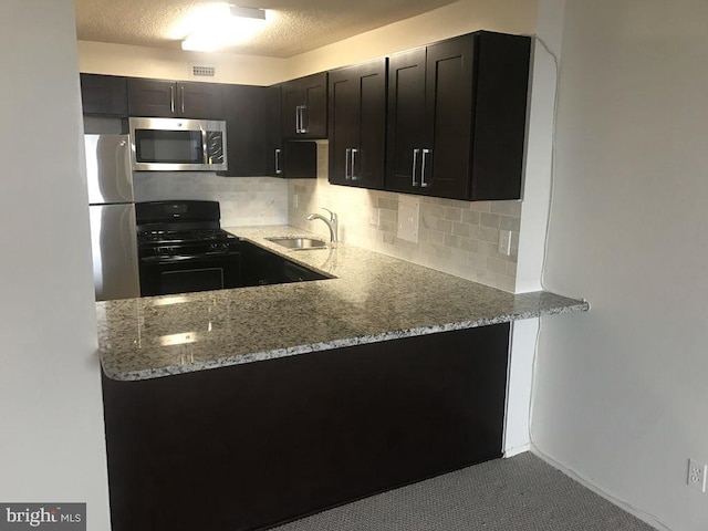 kitchen featuring light stone countertops, a textured ceiling, stainless steel appliances, and sink