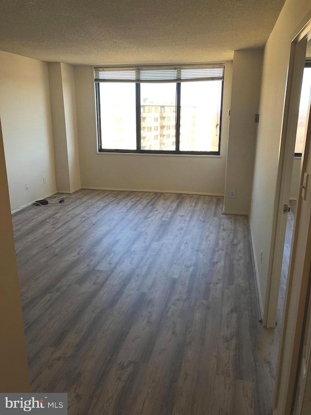 unfurnished room with a textured ceiling, a healthy amount of sunlight, and dark hardwood / wood-style floors