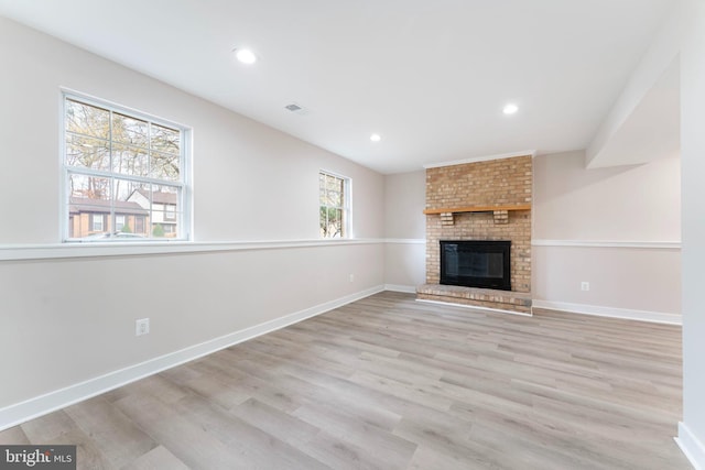 unfurnished living room with light hardwood / wood-style floors, a wealth of natural light, and a brick fireplace