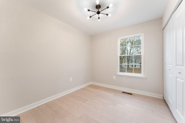 unfurnished bedroom with light wood-type flooring, a closet, and a notable chandelier