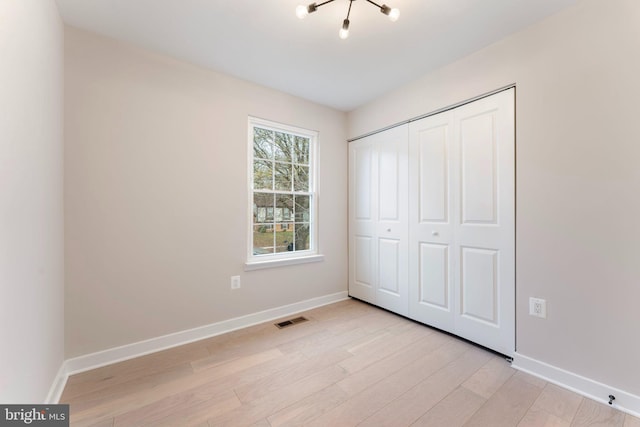 unfurnished bedroom featuring an inviting chandelier, light wood-type flooring, and a closet