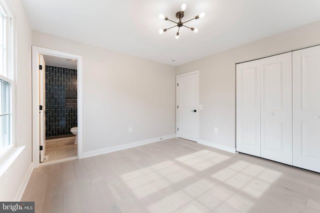 unfurnished bedroom with an inviting chandelier, light wood-type flooring, connected bathroom, and a closet