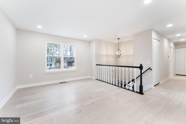 spare room with a notable chandelier and light wood-type flooring