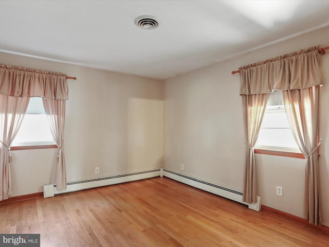 empty room featuring a healthy amount of sunlight, baseboard heating, and light hardwood / wood-style flooring