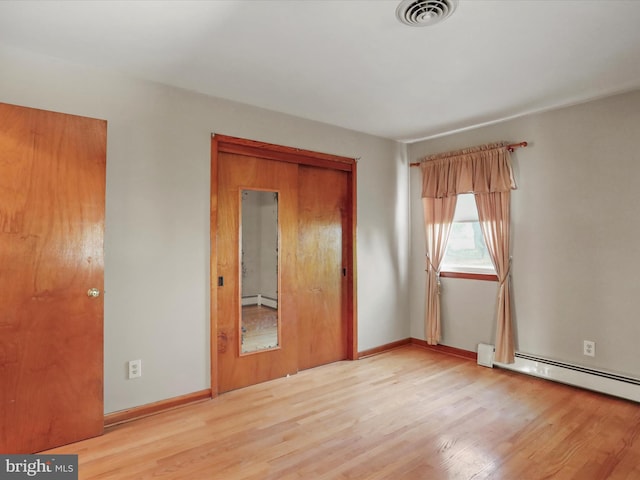 unfurnished bedroom featuring a closet, light hardwood / wood-style floors, and a baseboard heating unit