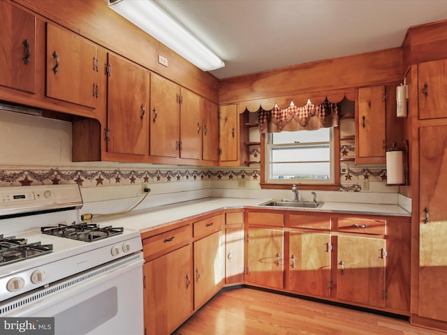 kitchen featuring white gas stove, light hardwood / wood-style floors, decorative backsplash, and sink