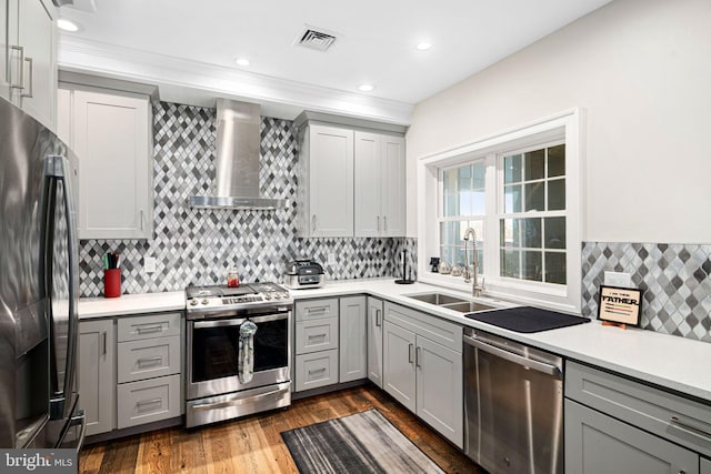 kitchen with wall chimney range hood, sink, hardwood / wood-style flooring, gray cabinets, and stainless steel appliances