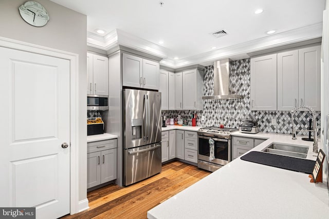 kitchen featuring decorative backsplash, appliances with stainless steel finishes, light wood-type flooring, sink, and wall chimney range hood