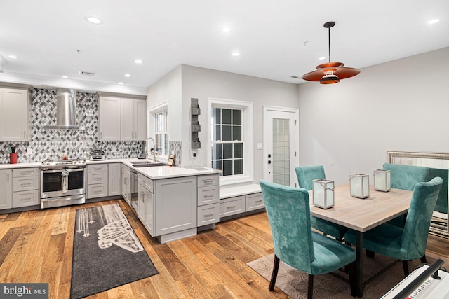 kitchen featuring pendant lighting, sink, wall chimney exhaust hood, kitchen peninsula, and stainless steel appliances