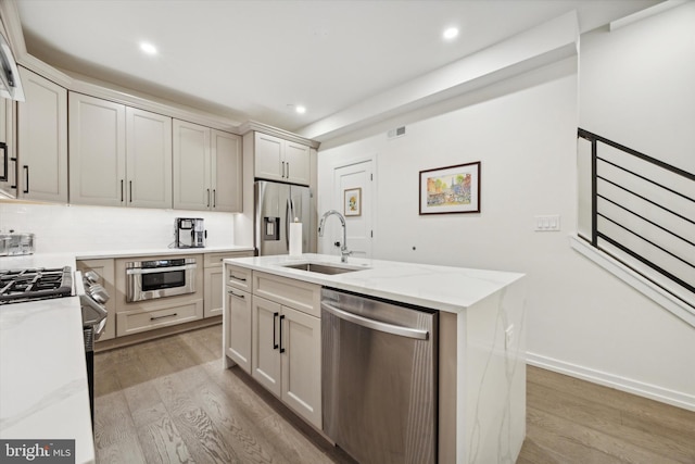 kitchen featuring a kitchen island with sink, sink, light hardwood / wood-style flooring, light stone countertops, and appliances with stainless steel finishes