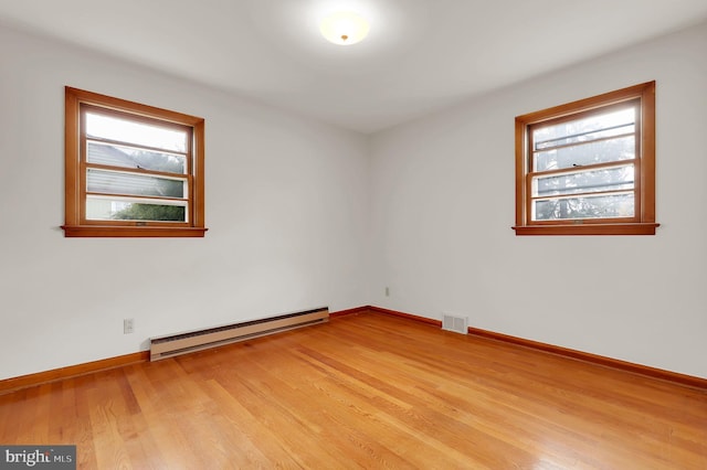 empty room featuring plenty of natural light, light hardwood / wood-style flooring, and a baseboard heating unit