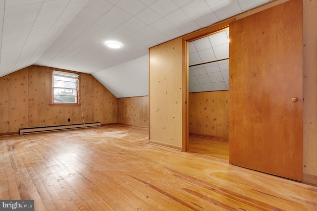 additional living space with baseboard heating, wooden walls, lofted ceiling, and light wood-type flooring