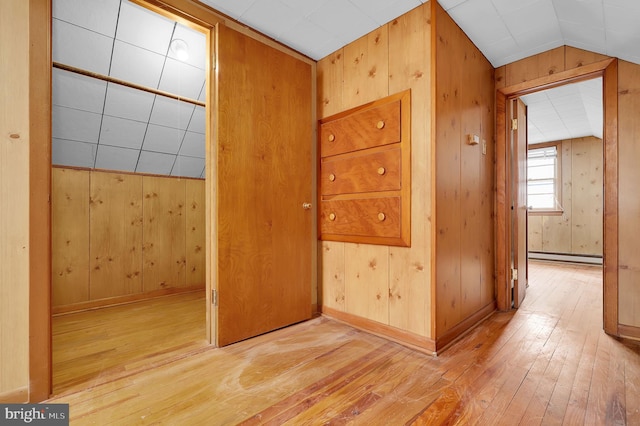 corridor featuring light wood-type flooring, vaulted ceiling, a baseboard heating unit, and wood walls