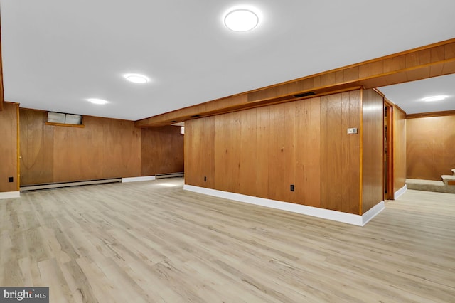 basement featuring wooden walls, a baseboard heating unit, and light wood-type flooring