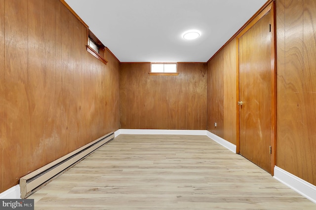 basement featuring light hardwood / wood-style floors, wooden walls, and a baseboard heating unit