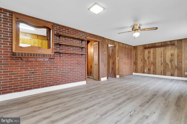 spare room featuring ceiling fan, brick wall, wooden walls, and light hardwood / wood-style flooring