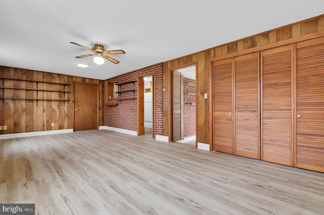 unfurnished bedroom featuring wood walls, ceiling fan, light hardwood / wood-style floors, and brick wall