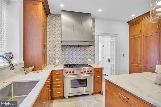 kitchen with custom exhaust hood, sink, tasteful backsplash, premium stove, and light stone counters