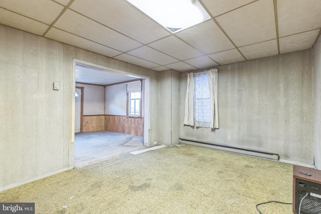 carpeted spare room featuring baseboard heating, a paneled ceiling, and wooden walls