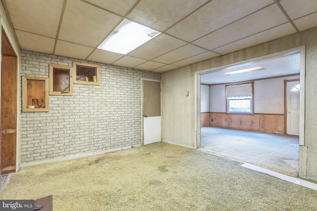 carpeted spare room with a paneled ceiling, wood walls, and brick wall