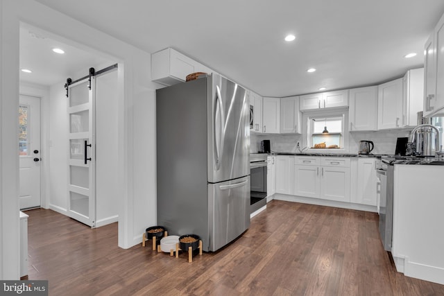 kitchen featuring dark wood-type flooring, a barn door, decorative backsplash, white cabinets, and appliances with stainless steel finishes