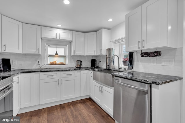 kitchen with stainless steel appliances, white cabinetry, dark wood-type flooring, and dark stone countertops