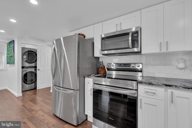 kitchen with dark hardwood / wood-style flooring, white cabinets, stacked washing maching and dryer, and appliances with stainless steel finishes