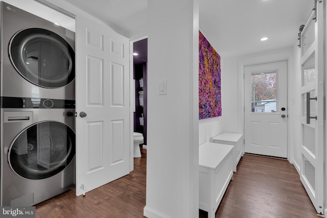 laundry room with dark hardwood / wood-style floors, a barn door, and stacked washer and dryer