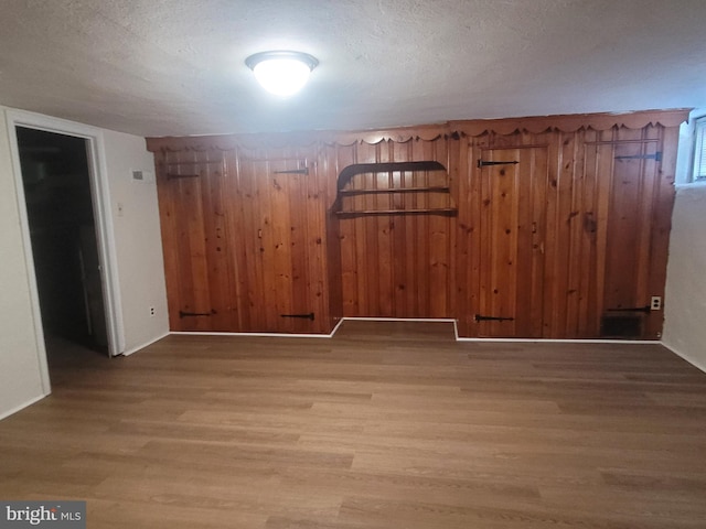 unfurnished room with a textured ceiling, light hardwood / wood-style flooring, and wood walls