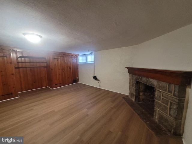 basement with a stone fireplace, wood-type flooring, and a textured ceiling