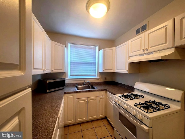 kitchen with refrigerator, sink, white gas range, light tile patterned floors, and white cabinetry