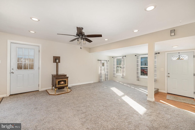 unfurnished living room with carpet floors, a wood stove, and ceiling fan