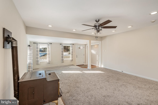 unfurnished living room with ceiling fan, light colored carpet, and a wood stove