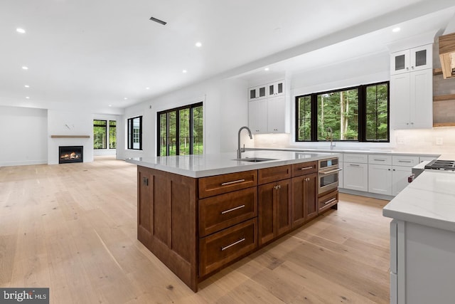 kitchen with tasteful backsplash, light stone counters, a kitchen island with sink, sink, and white cabinetry