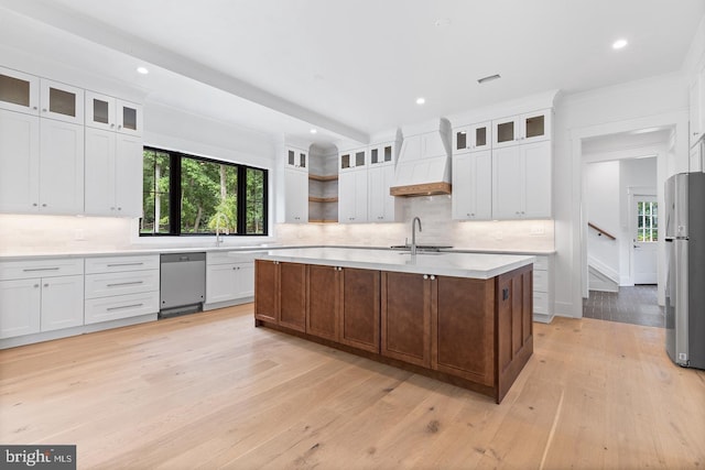 kitchen with light hardwood / wood-style flooring, a center island with sink, white cabinets, custom range hood, and appliances with stainless steel finishes