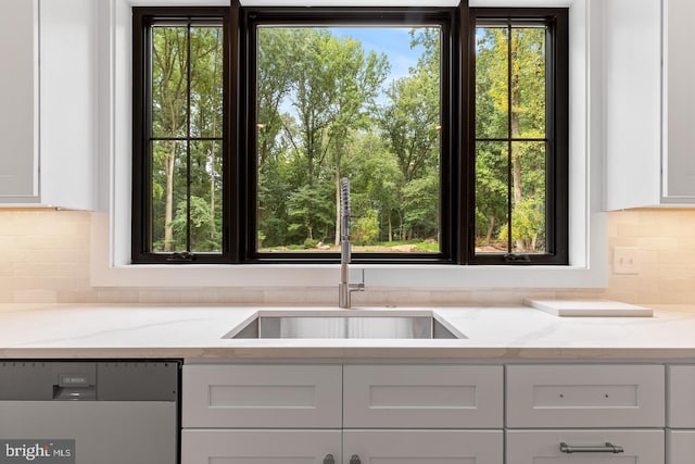 kitchen featuring dishwasher, light stone counters, white cabinetry, and sink