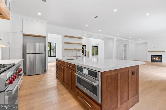 kitchen with white cabinetry, sink, stainless steel appliances, an island with sink, and a fireplace