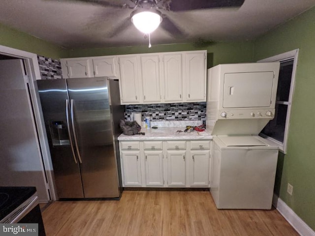 kitchen with stainless steel fridge, white cabinetry, stacked washer and dryer, and light hardwood / wood-style flooring