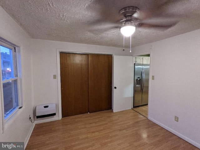 unfurnished bedroom with ceiling fan, light wood-type flooring, a textured ceiling, stainless steel fridge with ice dispenser, and a closet