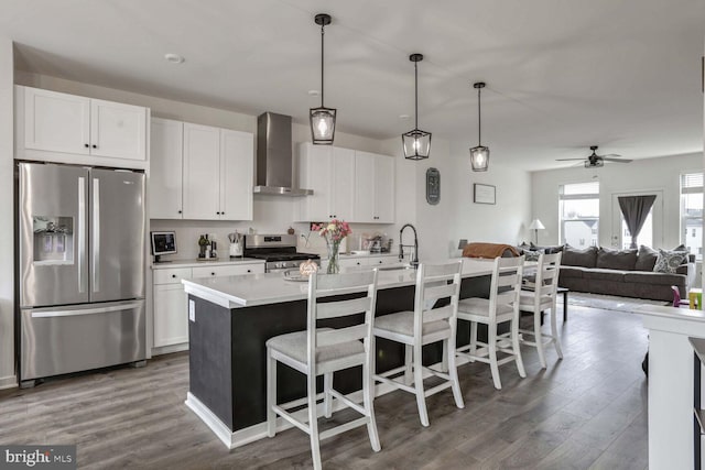 kitchen featuring wall chimney exhaust hood, white cabinetry, stainless steel appliances, and an island with sink