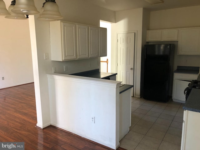 kitchen featuring dark hardwood / wood-style flooring, black refrigerator, white cabinets, and hanging light fixtures