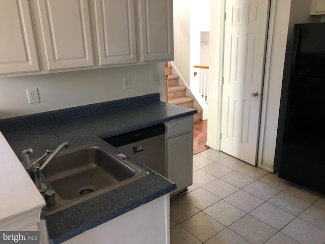 kitchen with white cabinets, black fridge, light tile patterned floors, and sink