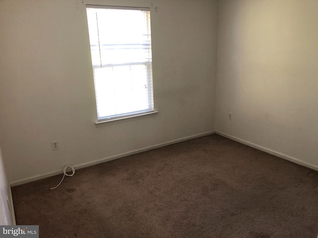 spare room featuring plenty of natural light and dark colored carpet