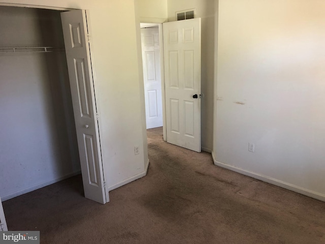 unfurnished bedroom with dark carpet and a closet