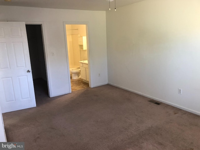 unfurnished bedroom featuring connected bathroom, a spacious closet, and dark colored carpet