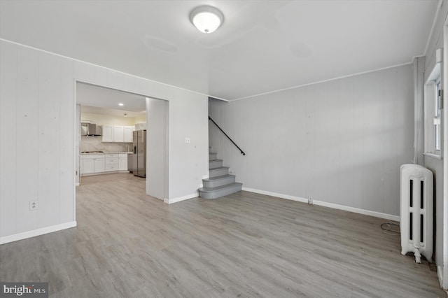 unfurnished living room with radiator heating unit, light hardwood / wood-style floors, and wood walls