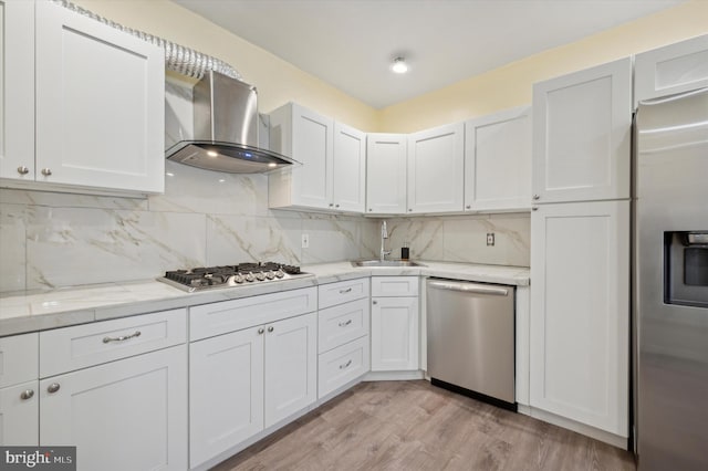 kitchen featuring white cabinetry, sink, stainless steel appliances, wall chimney range hood, and light wood-type flooring