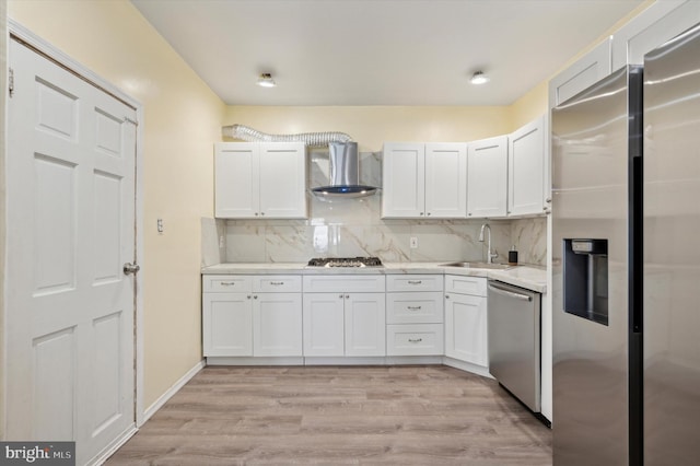 kitchen with white cabinets, stainless steel appliances, wall chimney range hood, and light hardwood / wood-style floors