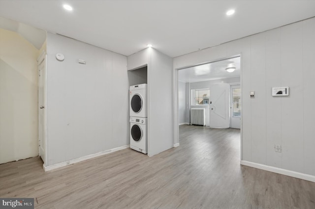 laundry area with stacked washing maching and dryer, radiator, and light hardwood / wood-style flooring